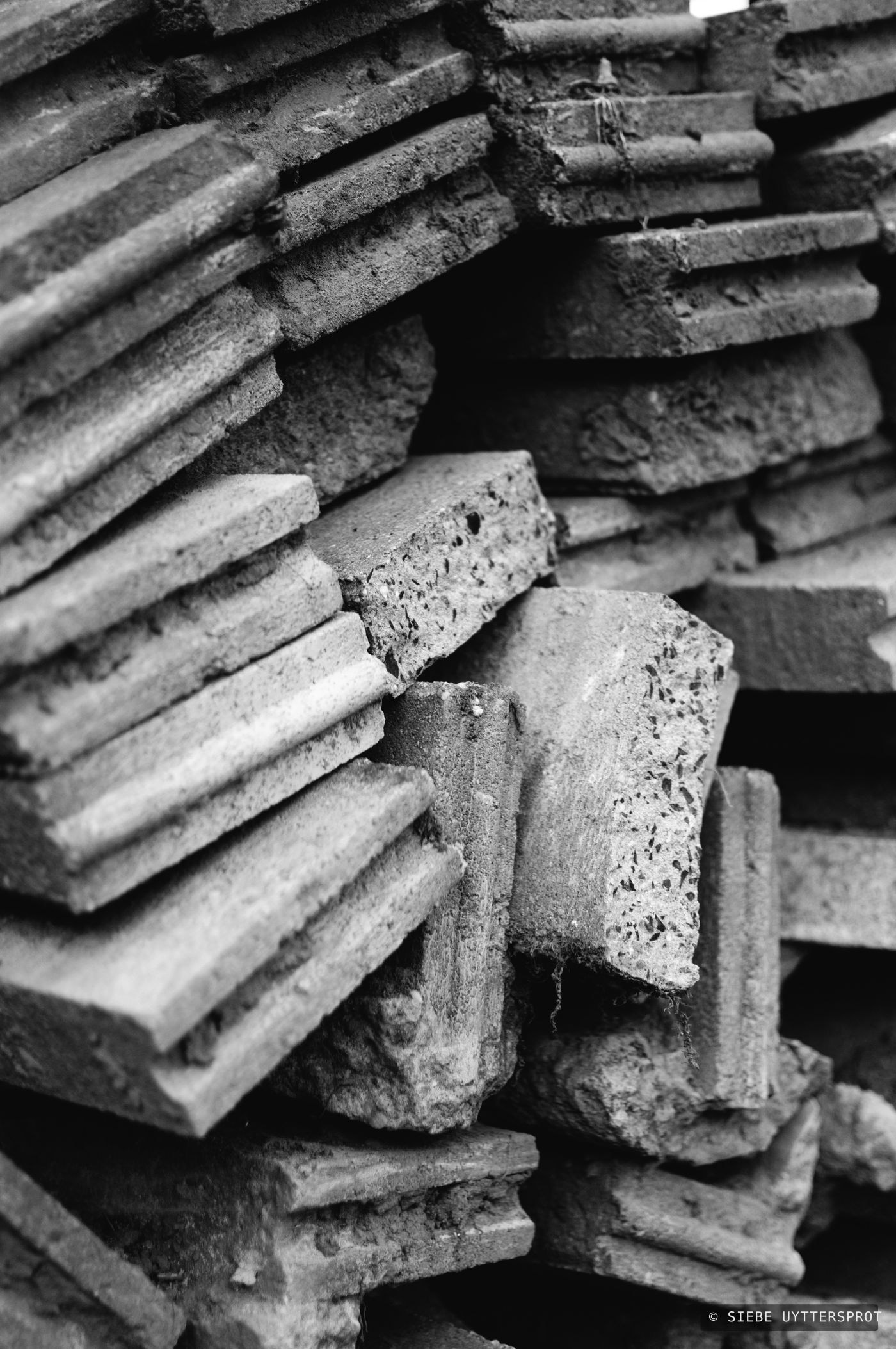 A close, portrait-orientation view of a weathered roof-tile stack, showing broken edges and pitted concrete texture.