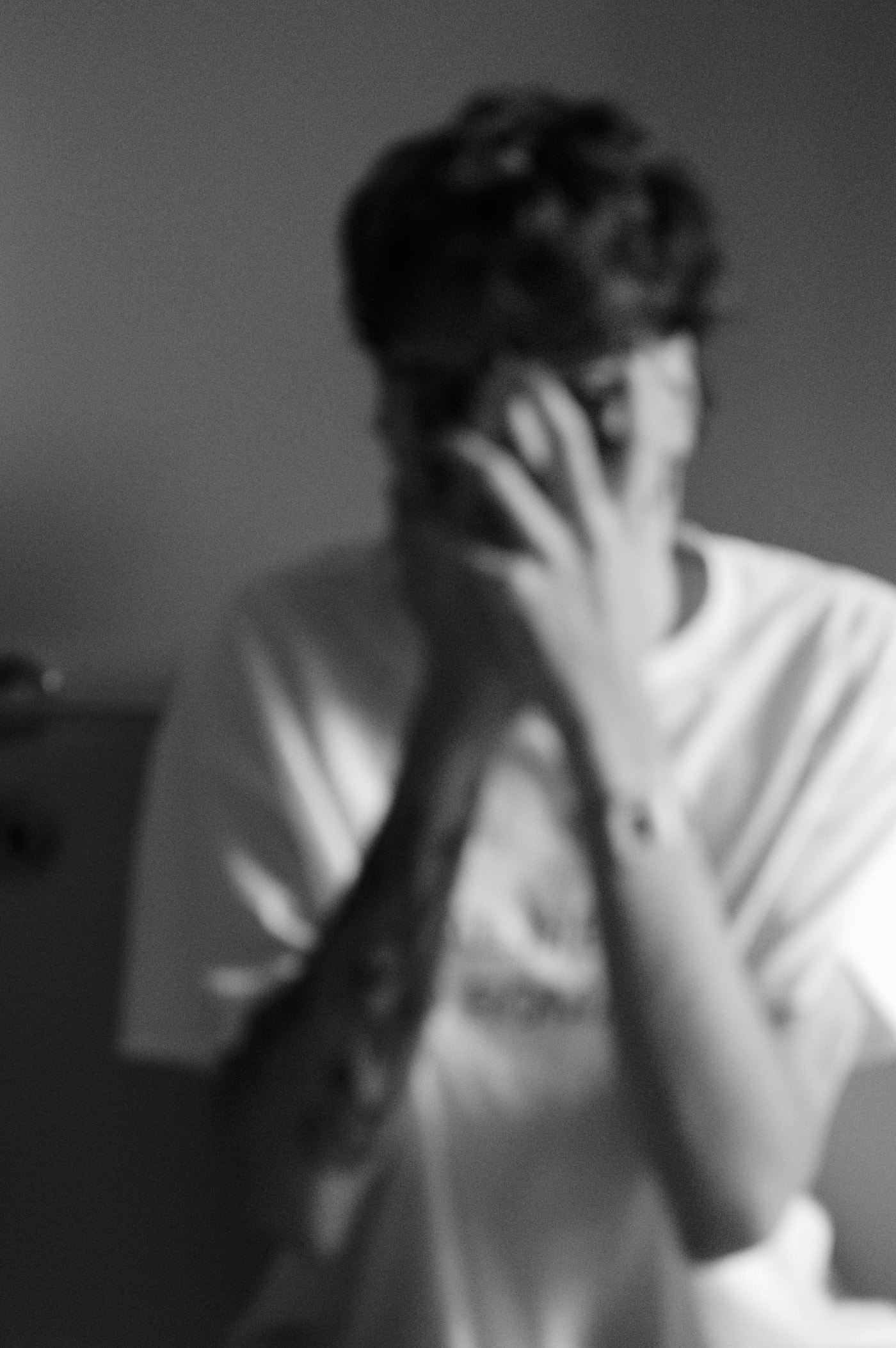 A blurred black-and-white self-portrait, phone held up to the ear, face obscured by a raised hand.